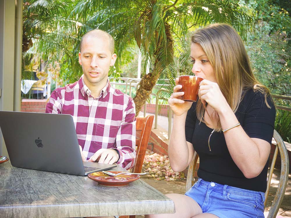 Illustratie van de Digital Soulmate die achter zijn laptop zit en iets bespreekt met een vrouwelijke klant die een kopje drinkt, ter visualisatie van een advies.